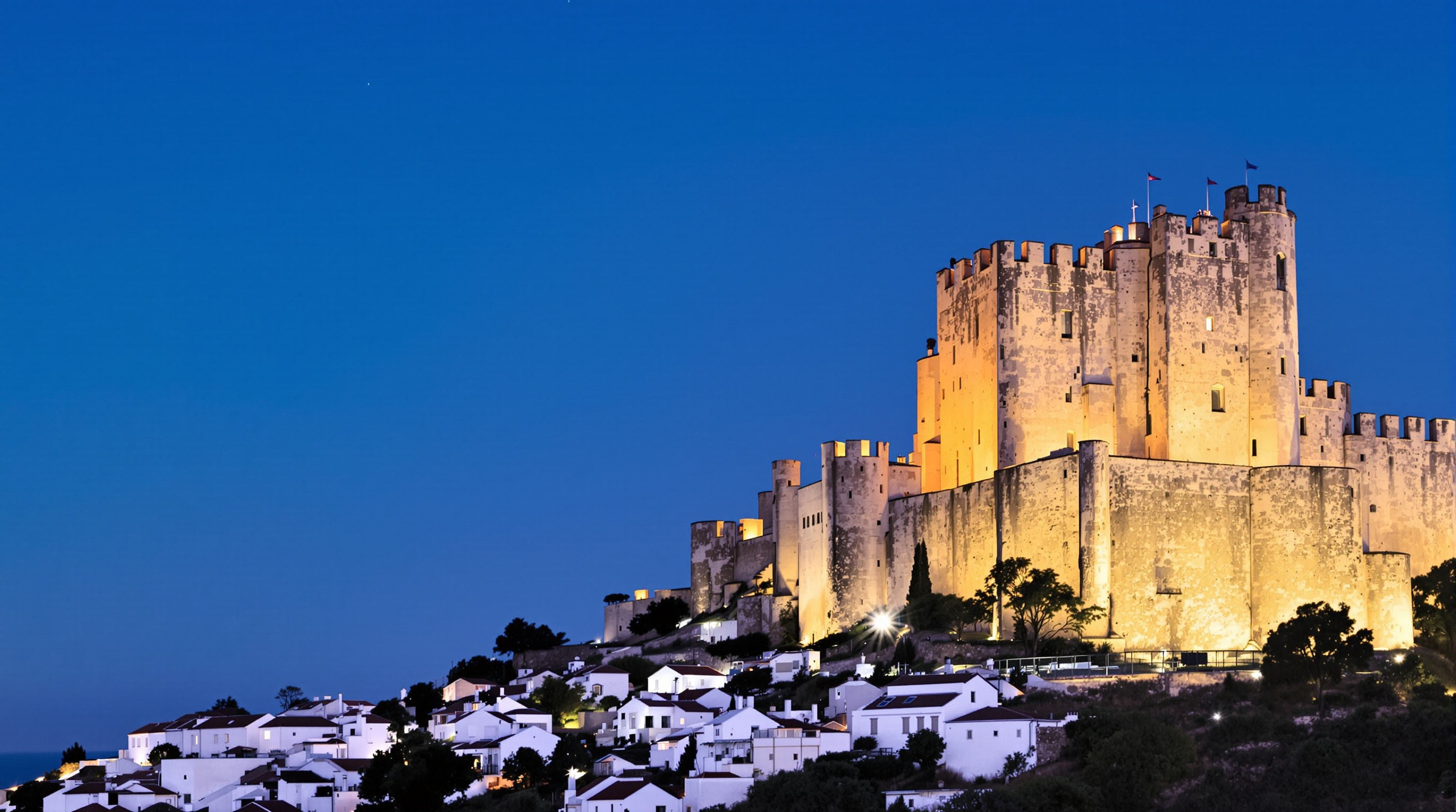 Floodlit medieval castle keep above a whitewashed Portuguese hill town at dusk